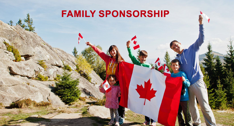 A family smiles and holds a Canadian flag outdoors. They wear casual clothing and footwear