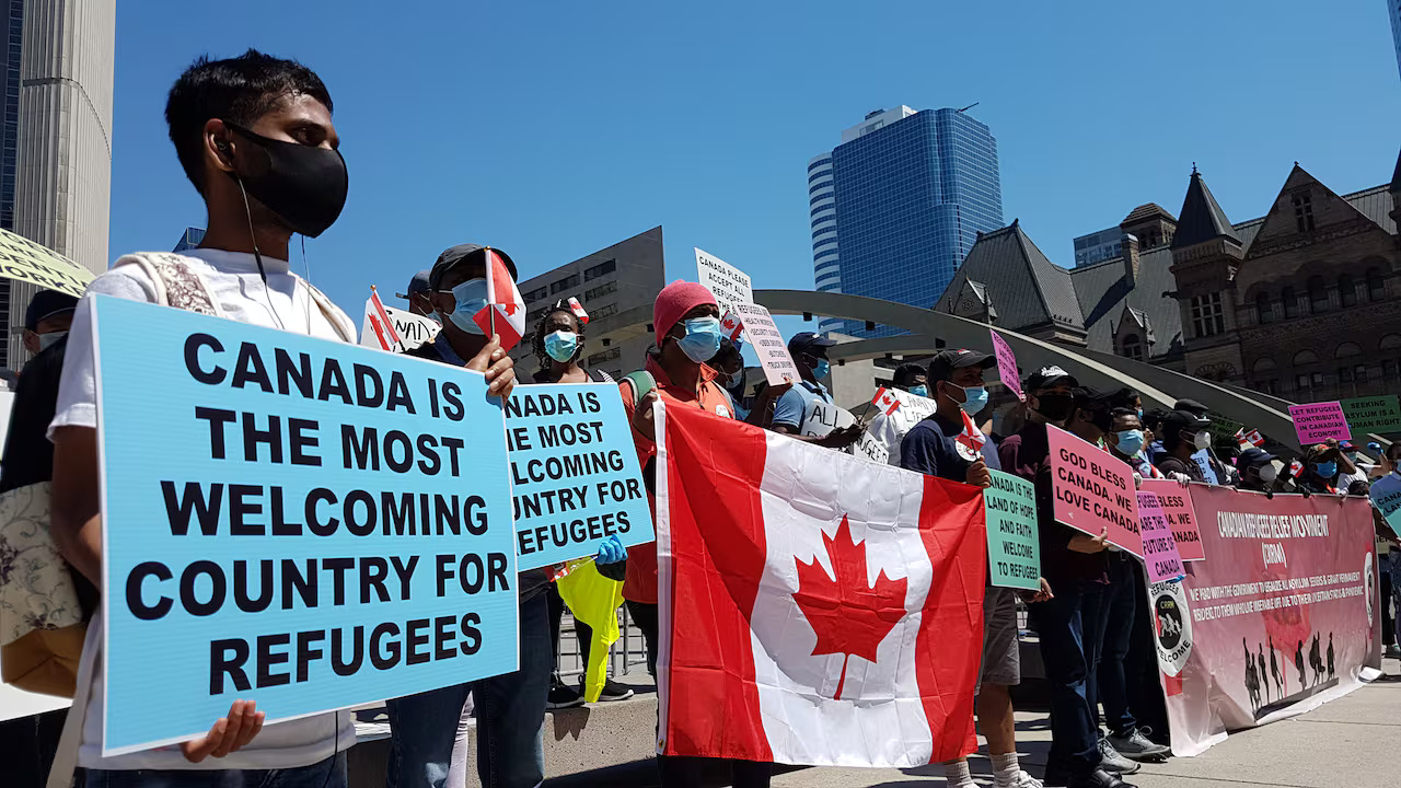 A group holds signs and flags welcoming refugees to Canada.